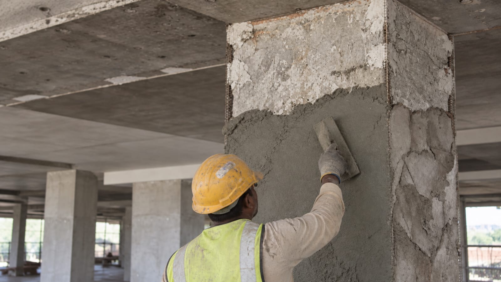 Applicator trowelling repair mortar onto a spalled concrete column with exposed reinforcement